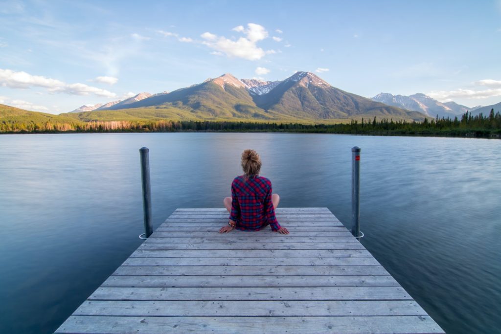 Photograph of a woman sitting on a lake pontoon looking out over the water.